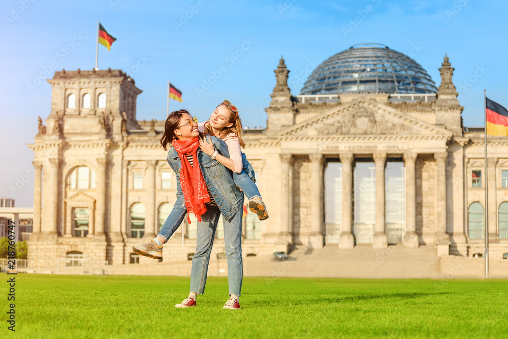 Fototapeta premium Dwa młodej studenckiej dziewczyny ma zabawę, tana i piggybacking na trawie blisko sławnego punktu zwrotnego w Berlin - Bundestag budynek. Koncepcja podróży