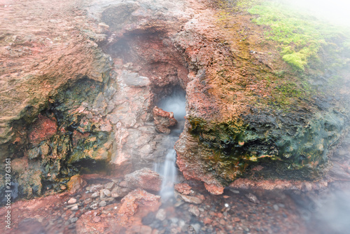 Closeup of steam geyser in Deildartunguhver hot springs in Iceland with cloudy mist fog long smooth exposure coming out of red rock colorful cave boiling water steam photo