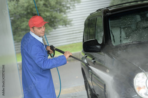 man working with high pressure washer to clean a car