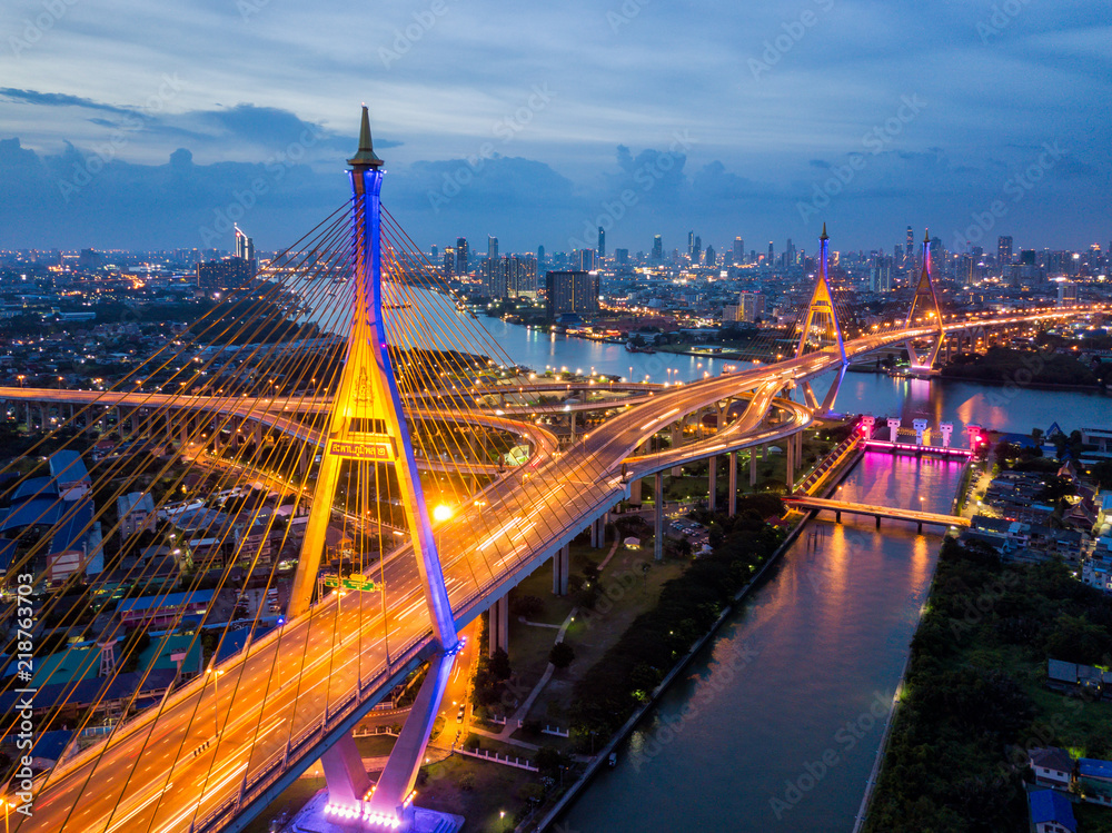 Fototapeta premium Aerial view of Bhumibol suspension bridge cross over Chao Phraya River in Bangkok city with car on the bridge at sunset sky and clouds in Bangkok Thailand.