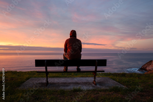 Lonely man sits alone on the rocky coast and enjoying sunset. View over rocky cliff to ocean horizon © Nickolay Khoroshkov