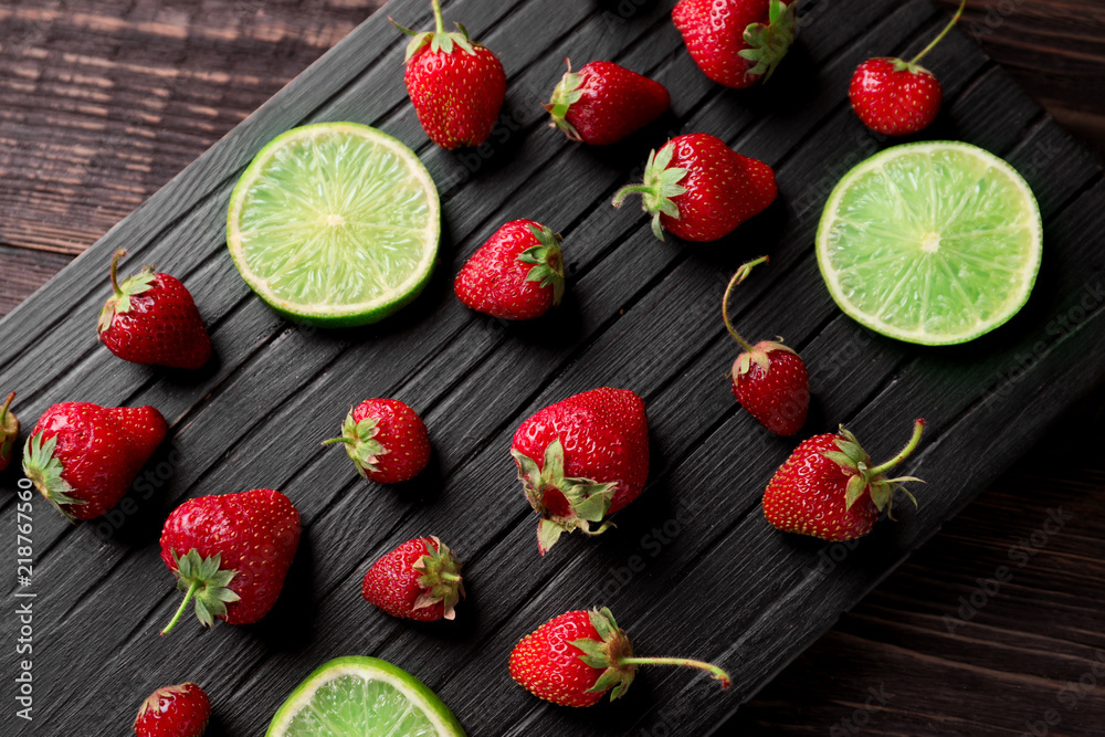 Ripe red strawberries with lime slices on wooden board