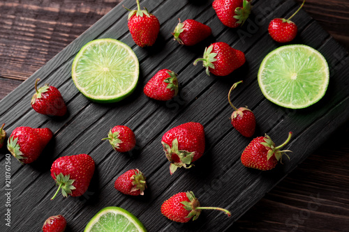 Ripe red strawberries with lime slices on wooden board