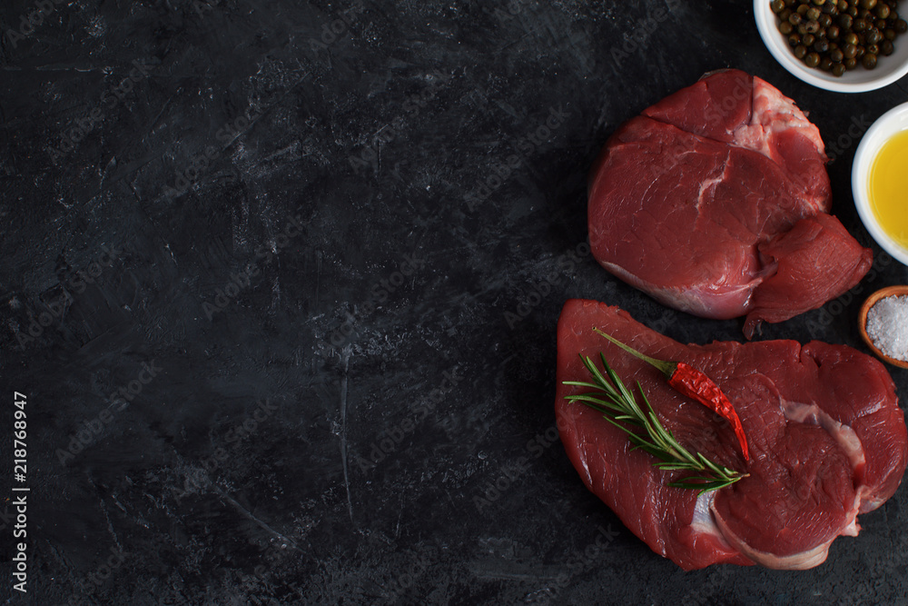 Fresh raw meat beef steak olive oil Spices Salt Wooden spoon Chili Pepper Rosemary Cooking concept Cooking concept Dark concrete background Top view Copy space Flat lay