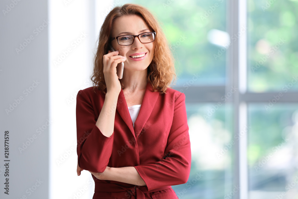 Successful businesswoman talking by mobile phone near window in office Successful businesswoman talking by mobile phone near window in office