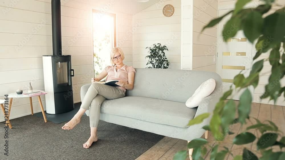 Intelligent young woman reading an interesting book, spending free time in spacious living room and enjoying the hobby during summer vacation Intelligent young woman reading an interesting book, spending free time in spacious living room and enjoying the hobby during summer vacation