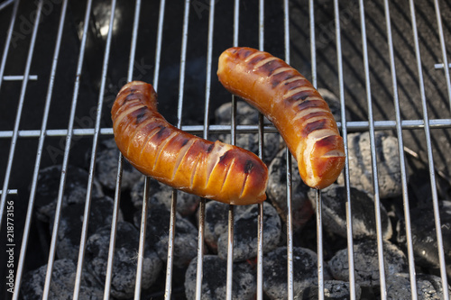 Two deliciously-looking sausages on a grill that warms on briquettes in Finland.