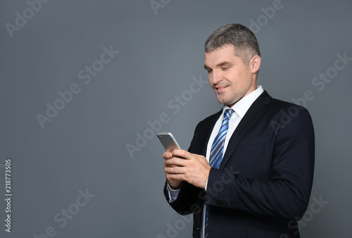 Handsome businessman with mobile phone on grey background © Pixel-Shot