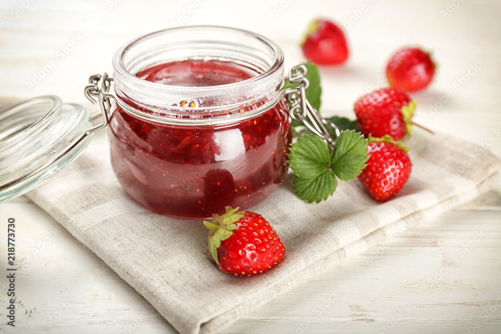 Glass jar with delicious strawberry jam on white wooden table Glass jar with delicious strawberry jam on white wooden table