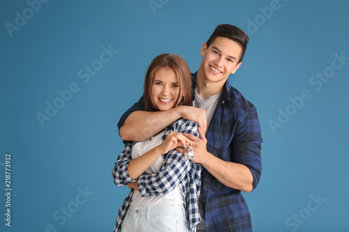 Young couple with key from their new house on color background