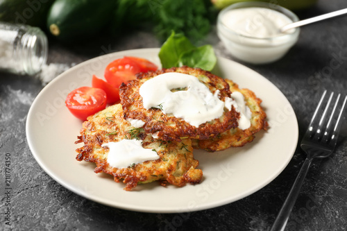 Plate with zucchini pancakes and sauce on table