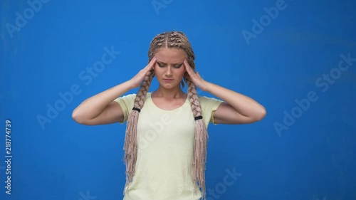 Fatigue stressful young female model keeps hands on head, closes eyes and opens mouth in desperation, has terible headache, isolated over blue background. Tiredness and exasperation concept photo
