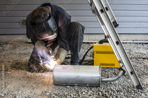 Man is welding pipes in Finland. He has dirty overalls and a welding helmet.