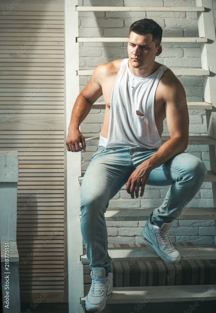 Guy in trendy tank top and jeans fashion. Young man sit on ladder. Athletic  macho with muscular chest and hands. Fashion model with stylish hair. Mens  fashion style and trend Stock Photo