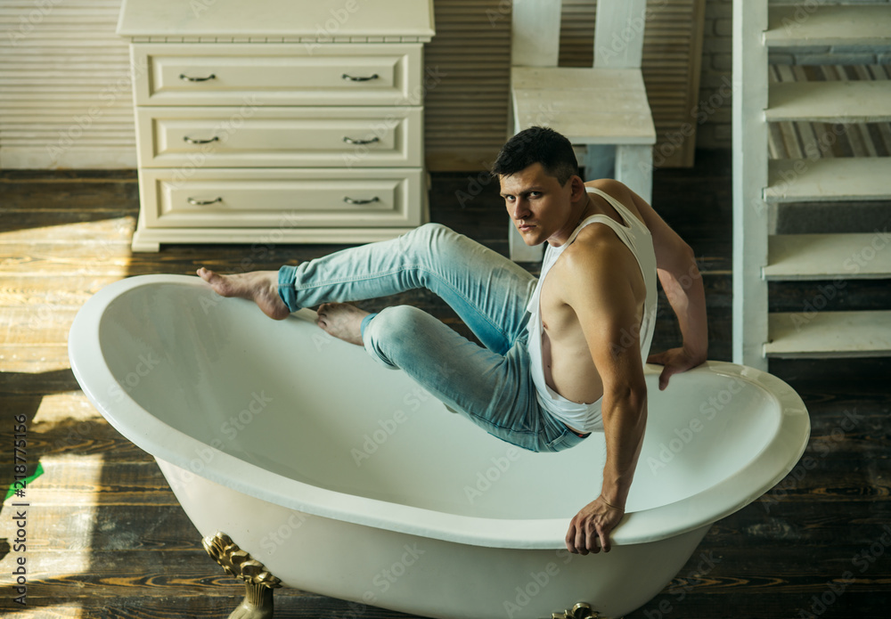 Guy sit on bath. Man in bathroom. Sexy macho in tank top and jeans fashion.  Fitness model with strong body health. Hygiene and bathing concept Stock  Photo | Adobe Stock