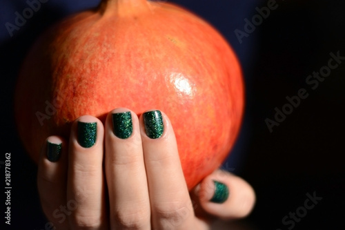 Beautiful big pomegranate in girl's hands with green manicure