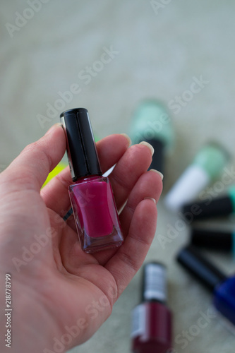 pink nail polish bottle in woman's hand on the background of other colorful bottles
