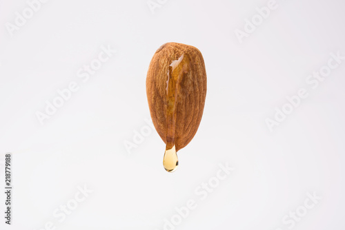 Golden almond oil drop dripping from while Badam dry fruit, flying in the air isolated