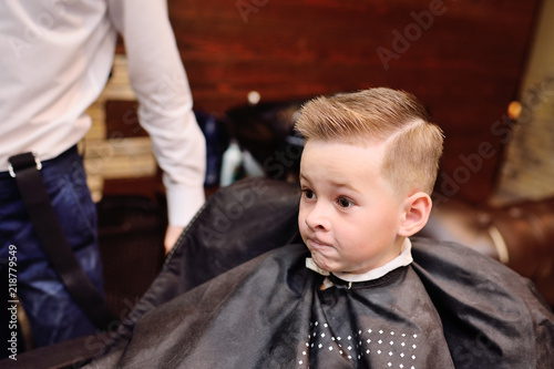 little baby boy in a barber's chair looks at his haircut in the mirror
