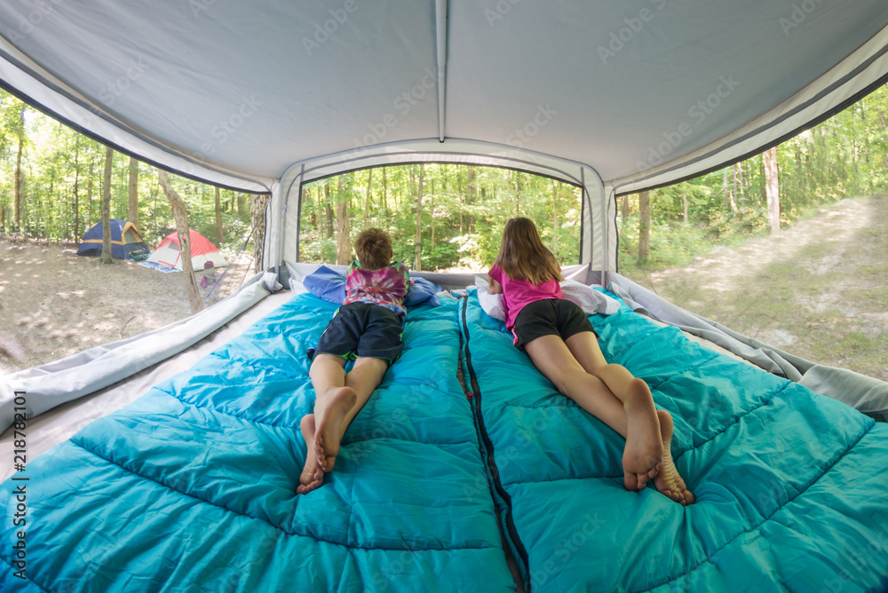 Bare footed children laying on blue sleeping bags in popup camper bunk