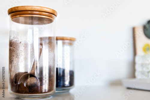 Closeup of two kitchen spices closed glass jars with wooden lids, coffee, cocoa, or cinnamon, measuring, measurement spoon inside, reflection © Andriy Blokhin