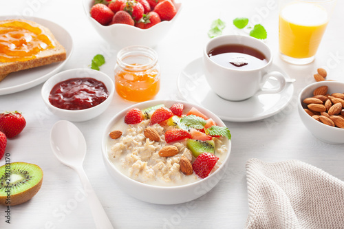 healthy breakfast with oatmeal porridge, strawberry, nuts, toast, jam and tea