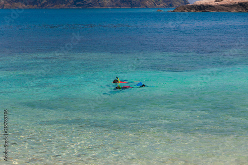 Two tourists snorkelling in the turquoise blue sea, in front of the shallow clear waters of Rawa beach, an island near Perhentian Kecil in Malaysia.