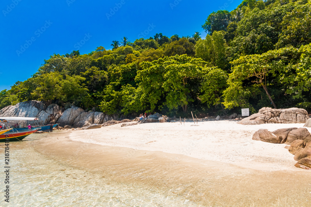 The powdery white sandy beach surrounded by rocks & trees, tourists resting in the shade and boats floating on the glimmering shallow water of Pulau Rawa, makes it a nice holiday scene near Perhentian