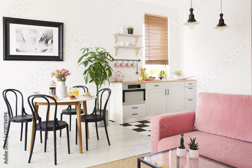 Photos Pink sofa in white apartment interior with kitchenette and black chairs at dining table