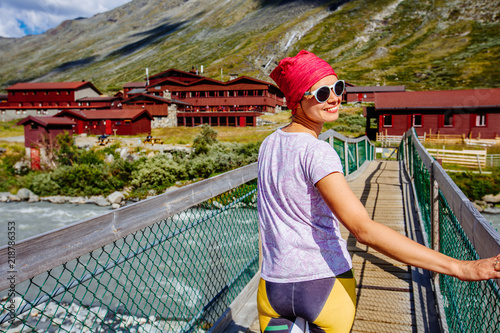 Sportive female tourist standing on bridge above river enjoying landscape in Jotunheimen national park Norway Travel scandinavian scenery. photo