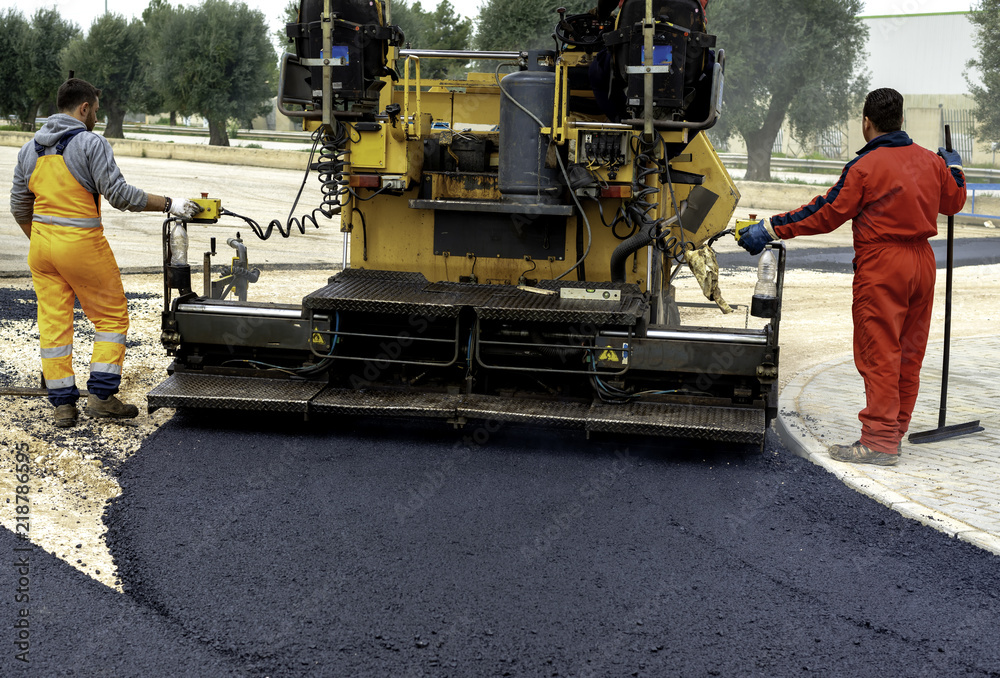 Workers regulate tracked paver laying asphalt heated to temperatures above 160 ° pavement on a runway Workers regulate tracked paver laying asphalt heated to temperatures above 160 ° pavement on a runway