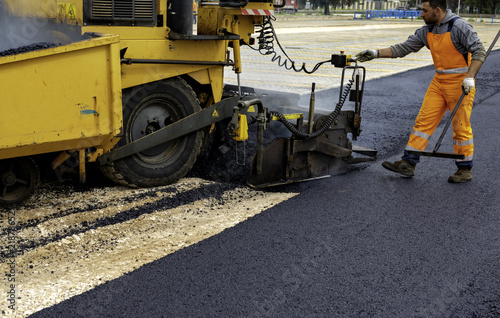 Machine operator to spread asphalt, intervenes on the control panel to adjust the asphalt paving