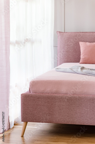 Dirty pink, comfy bed by a window with sheer curtains in a bright bedroom interior © Photographee.eu