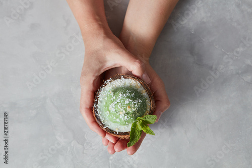 Womans hands take a halh of coconur with tasty homemade green ice cream with mint leaf on a gray concrete. photo