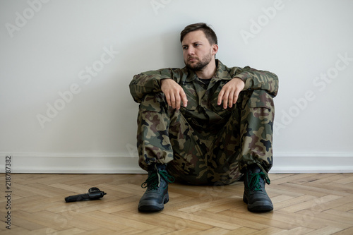 Tired professional soldier in green uniform sitting on the floor next to a gun