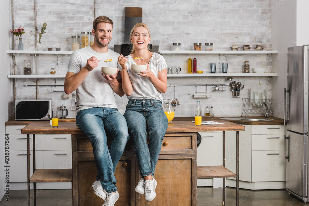 happy couple having breakfast and sitting on kitchen counter happy couple having breakfast and sitting on kitchen counter