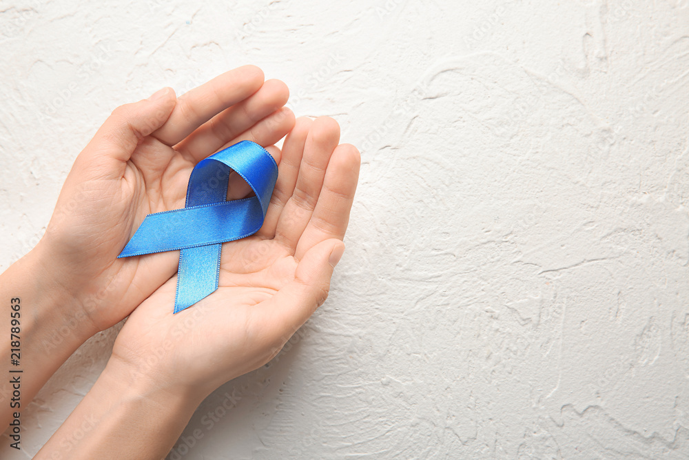 Woman holding blue ribbon on light background. Cancer concept Woman holding blue ribbon on light background. Cancer concept
