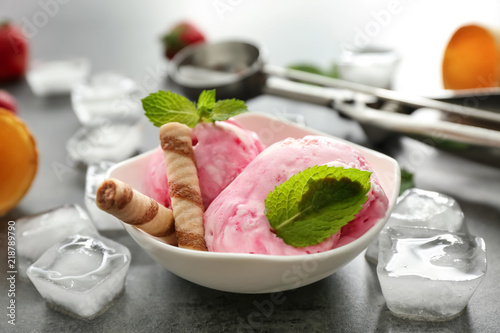 Bowl with delicious strawberry ice-cream and ice cubes on dark background, closeup