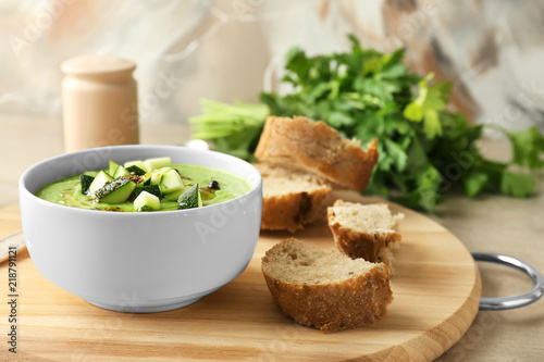 Tasty zucchini soup in bowl with bread on wooden board