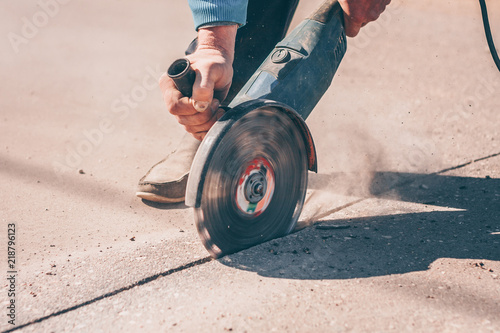 The worker saws the asphalt with an angular grinder with a diamond disc before carrying out repair and repair work photo