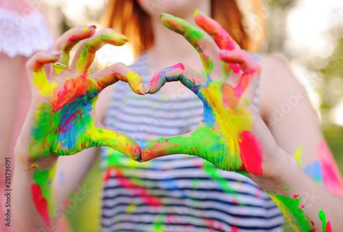 the girl with the hands smeared with colored fingers shows the heart on the background of nature and the sun