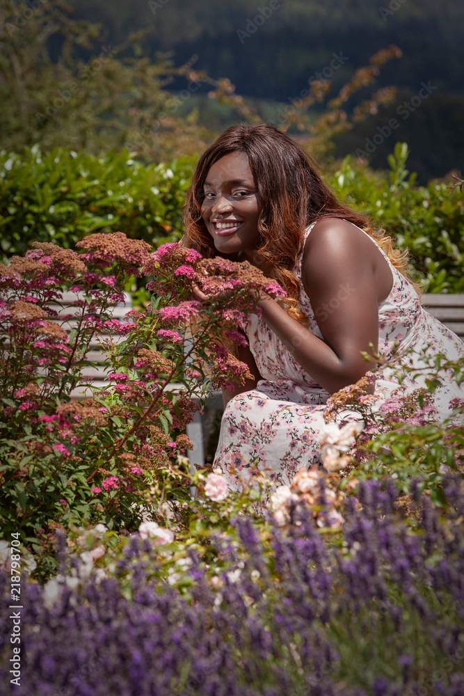 Junge kurvige Frau in einem Sommerkleid genießt den Duft der Blumen Junge kurvige Frau in einem Sommerkleid genießt den Duft der Blumen