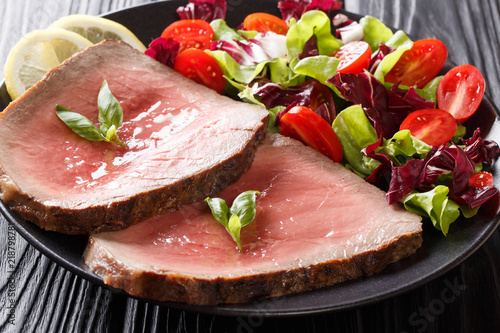 Sliced grilled beef steak with fresh vegetable salad close-up on a black background. horizontal