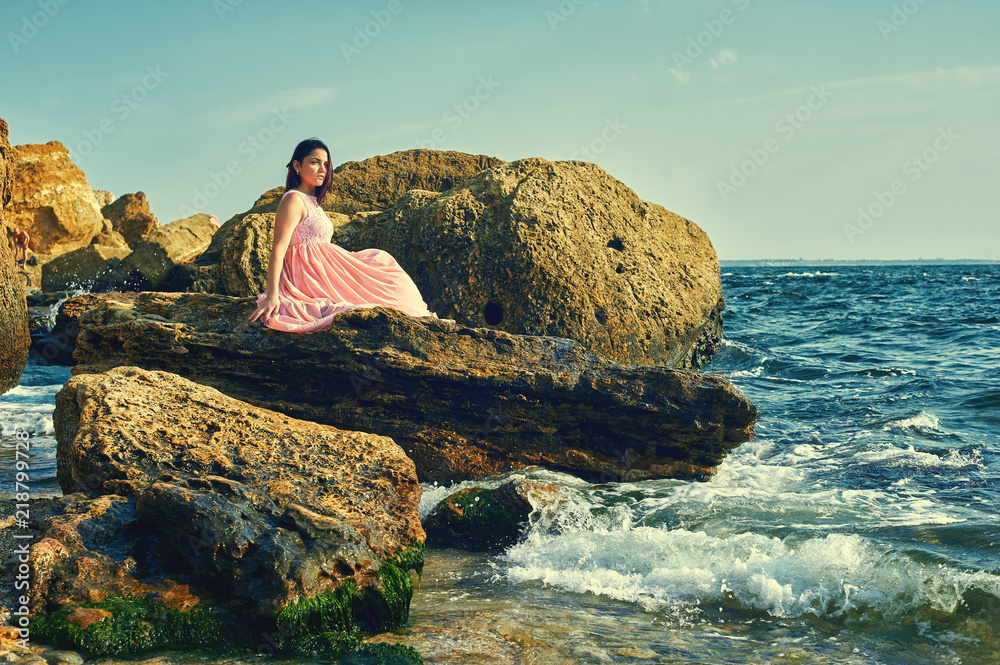 Young girl resting on the rocks by the sea . Woman enjoying the morning sea air