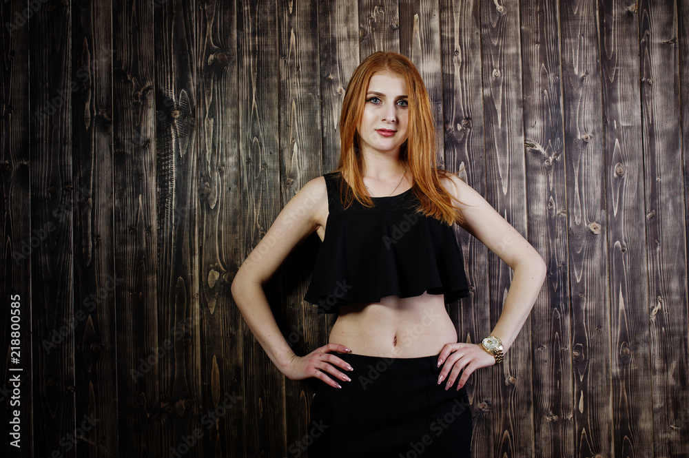 Portrait of a beautiful redheaded girl in black top and black skirt posing in the studio next to the wooden wall. Portrait of a beautiful redheaded girl in black top and black skirt posing in the studio next to the wooden wall.