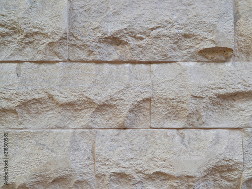 Decorative wall, built of hewn stone slabs of beige color, texture close-up