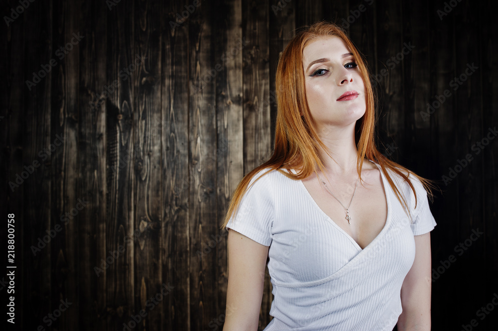 Portrait of a gorgeous redheaded girl in white t-shirt and denim shorts posing in the studio next to the wooden wall. Portrait of a gorgeous redheaded girl in white t-shirt and denim shorts posing in the studio next to the wooden wall.
