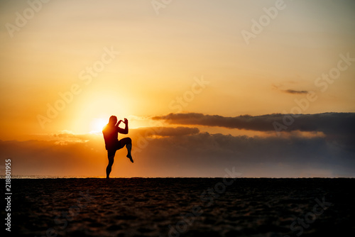 Silhouette of man practicing martial arts on beach.