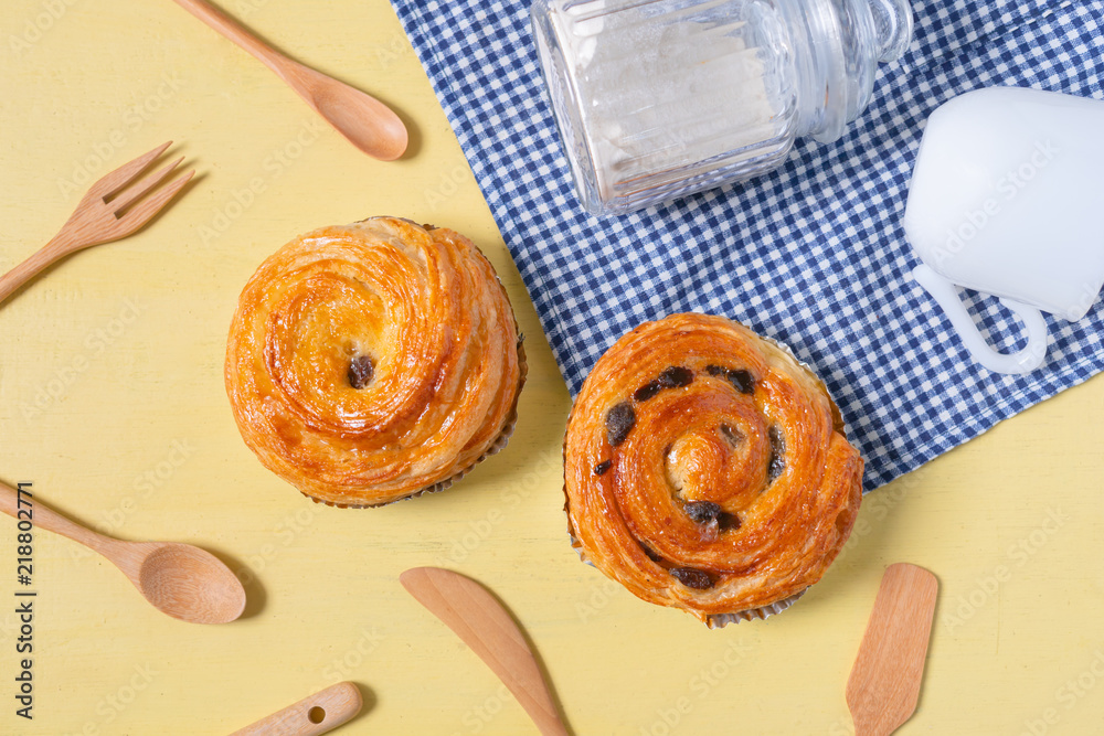 Raisin danish pastry on the yellow wood and blue gingham check cloth. Colourful tasty sweet bakery..