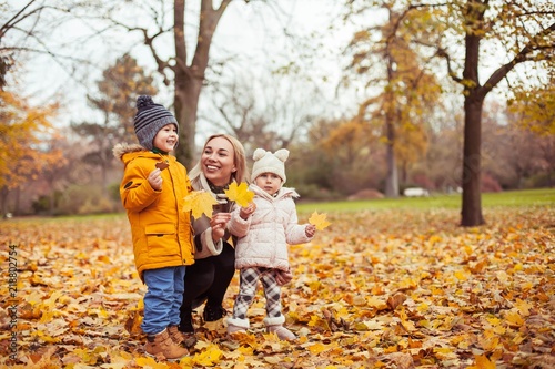 A young beautiful mother and two small children are walking around the autumn park. Mom and two small children play. Warm winter. Bright autumn.